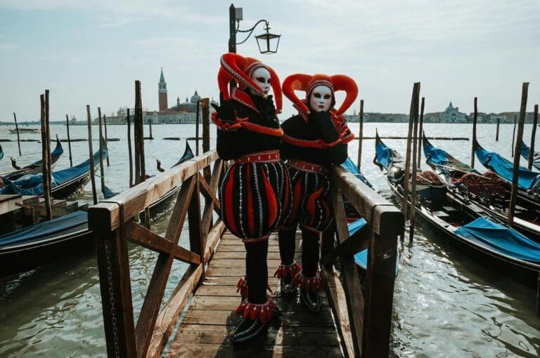 Two people in costume stand beside gondolas during carnival in Venice