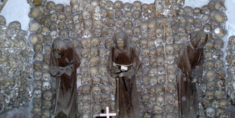 The Capuchin Crypt in Rome showing the skeletons of three robed friars in niches made from human skulls