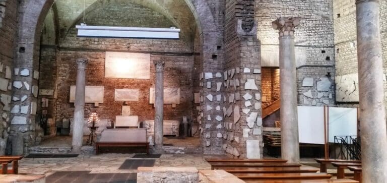 The underground church in the catacombs of Domitilla with ancient Roman columns and a view towards the altar with marble fragments of tomb covers on the walls