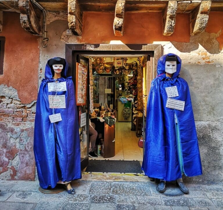 Shop front in Venice showing two mannequins dressed in purple robes wearing the Bauta style Venetian Carnival mask