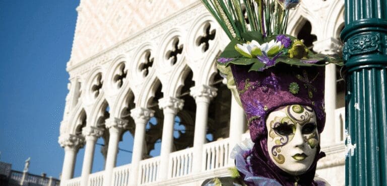Venetian Canival goer wearing as mask and purple hat with green foliage head-dress and a Venetian Palazzo in the background